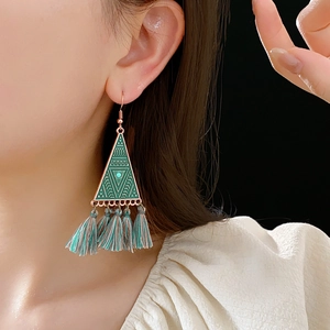 Detail of bohemian triangle earrings with green tassels worn by a model on dark background