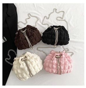 Detail of four drawstring bucket bags with metal chains and pearl accents on white fabric