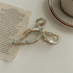 Detail of marble pattern acetate bow hair claw clip with gold metal spring on white desk