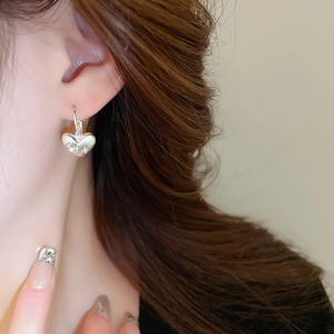 Close-up of heart-shaped silver earrings with sparkling zircon stones worn by model