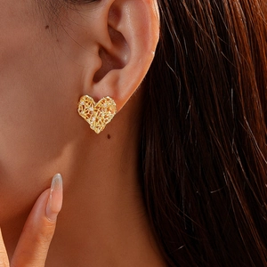 Close-up of golden hollow heart earrings with white zircons on a model's ear