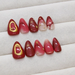 Deep red almond press-on nails with gold star patterns and metallic 3D rhinestones
