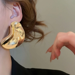 Close-up of oversized irregular liquid metal earrings in glossy gold on a model