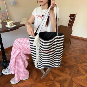 Detail of striped canvas tote bag featuring white lace trim and red embroidery accents