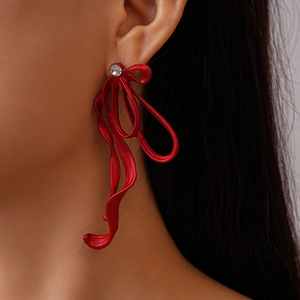 Close-up of a large red metal bow earring with rhinestones and long tassel detail