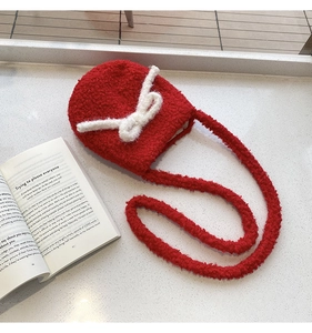 Detail of red plush crossbody bag with white bow accent on a stone surface