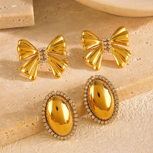 Gold bow earrings and oval rhinestone studs displayed on a premium stone surface