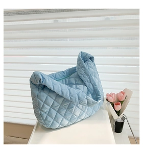 Detail of blue quilted puff shoulder bag on white surface with a tulip accent