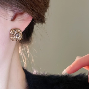 Detail showing square champagne gold stud earrings with diamonds on ear lobe