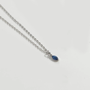 Macro shot of a silver necklace featuring a delicate blue marquise-cut gemstone pendant