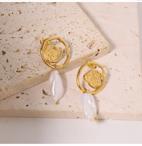 Macro detail of baroque natural pearl earrings with irregular gold rings on stone surface