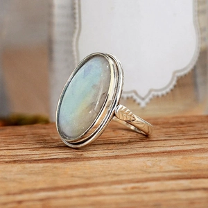 Detailed close-up of vintage oval moonstone ring with leaf textured silver band on wood