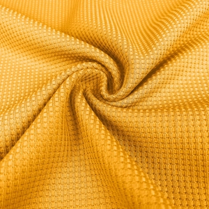Close-up of yellow knitted waffle texture fabric with a soft drape and spiral pattern