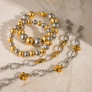 Bracciali e collane con perline oro e argento lucido su sfondo di pietra beige soft