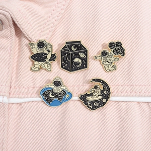 Detailed view of five creative astronaut enamel pins pinned on a pink denim jacket collar