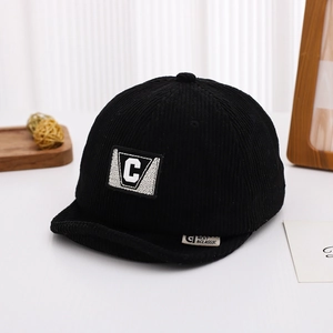Detail of black corduroy baby cap featuring letter C patch and textured fabric weave