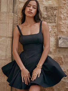 Detail view of a black backless mini dress with ruffles and straps against a stone wall