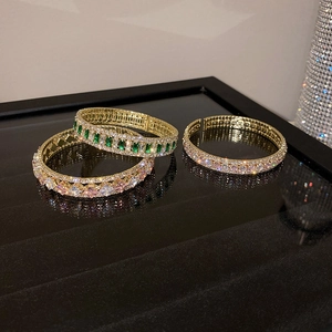 Detailed macro view of three gold-plated bangles with vibrant green and pink gemstones