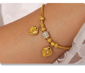 Nahaufnahme des goldenen Schlangenarmbands mit Herzanhängern und funkelnden Kristallen