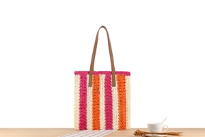 Detail of pink and orange striped woven tote with brown leather straps on a wooden table