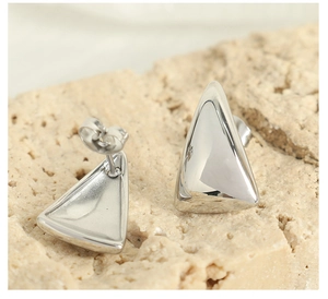 Detailed macro view of silver geometric triangle stud earrings on natural stone surface