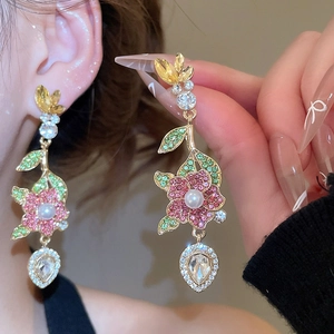 Dettaglio di orecchini a fiore dorati con petali di cristallo, perla e zircone a goccia