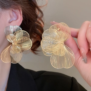 Détail de grandes boucles d'oreilles fleurs ajourées dorées montrant le travail du fil