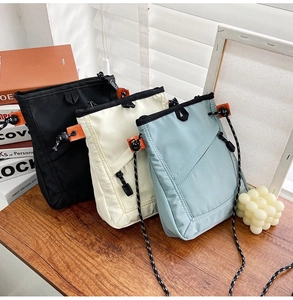Three nylon crossbody bags in black, beige, and light blue on a wooden table setup