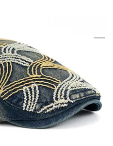 Macro detail of washed denim beret featuring yellow wavy embroidery and curved brim