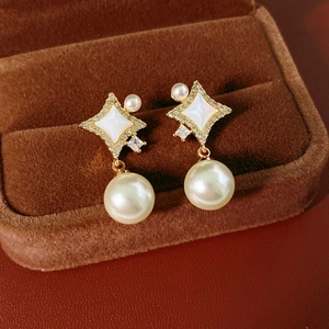 Détail de boucles d'oreilles étoile dorées avec incrustation nacre et grande perle ronde
