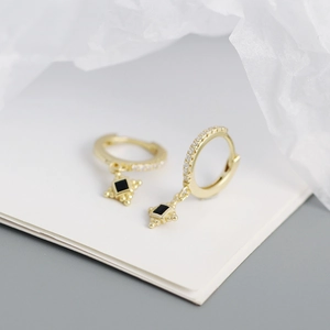 Detail shot of gold hoop earrings featuring square black gemstones and golden bead charms