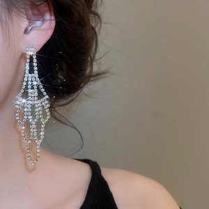 Macro view of geometric silver tassel earrings with sparkling rhinestones on a model