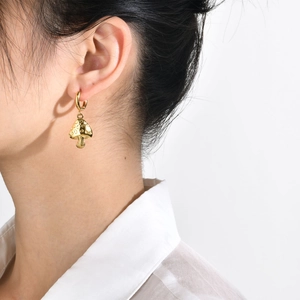 Close-up of a person wearing gold mushroom hoop earrings with a polished metallic finish