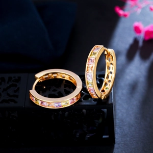 Macro shot of gold hoop earrings set with colorful square zircons on a black display