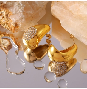 Détail des boucles d'oreilles goutte dorées serties de zircons sur surface miroir