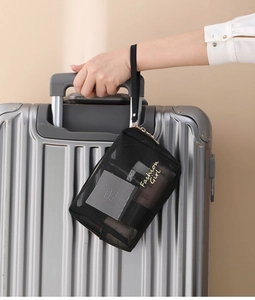 Detail of black mesh makeup bag with Fashion Girl embroidery hanging on a suitcase