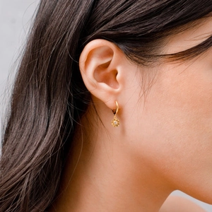 Nahaufnahme von goldenen Sonnenblumenohrringen mit Diamantbesatz, getragen von einem Modell