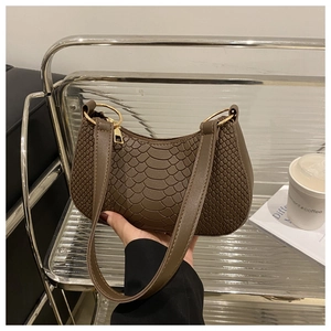 Detail of caramel brown croc-embossed baguette bag with metallic ring and slim strap