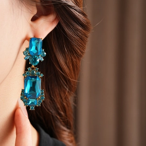 Close-up of vintage gold square earrings with blue gems worn by a model