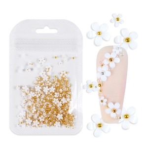 Detail showing white 3D resin flower nail charms with gold beads in bag and on nails