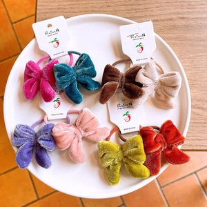 Detailed view of 8 colorful velvet bow hair ties displayed on a white plate