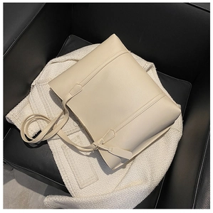 Close-up of a minimalist beige leather tote bag placed on a textured tweed jacket