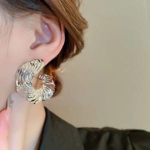 Close-up of irregular spiral C-shaped silver earrings with textured water ripple design