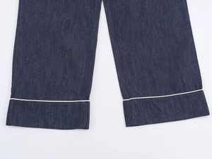 Detailed view of dark blue denim pant leg featuring contrast white piping trim
