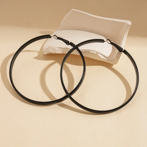 Macro view of large black geometric hoop earrings on textured minimalist background