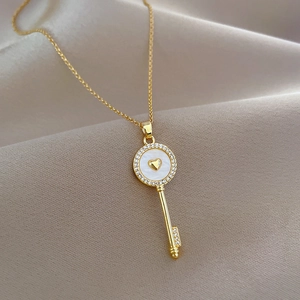Macro view of gold key necklace with white shell inlay and crystals on beige silk fabric