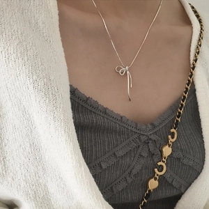 Close-up of a silver bow pendant necklace worn on a model with a snakeskin chain style