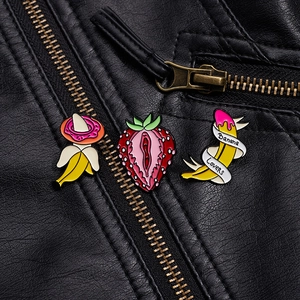Detail of banana and strawberry enamel pins on black leather jacket showing texture
