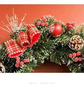 Detail of Christmas wreath with red plaid bow, pine cones, and snowy berry accents