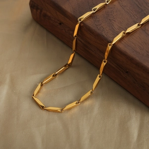 Two-tone bamboo geometric necklace in gold and steel finish displayed on wood